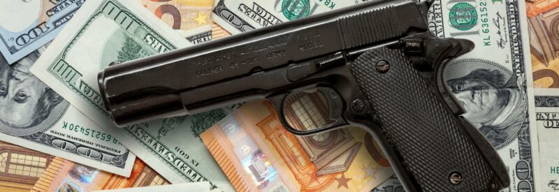 a hand gun resting on a pile of money that you could make if you sell guns