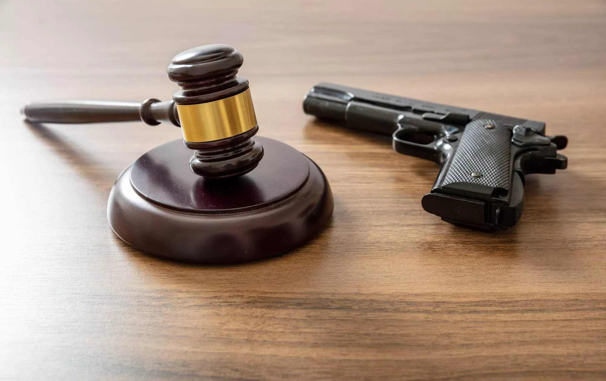 judge's gavel and gun on wooden desk symbolizing the question of how old do you have to be to buy a gun in the US