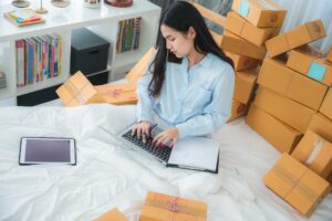 woman sitting on bed typing on a laptop while surrounded by boxes difference between ach and wire