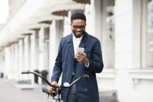 man looking at phone while walking a bike ach echeck
