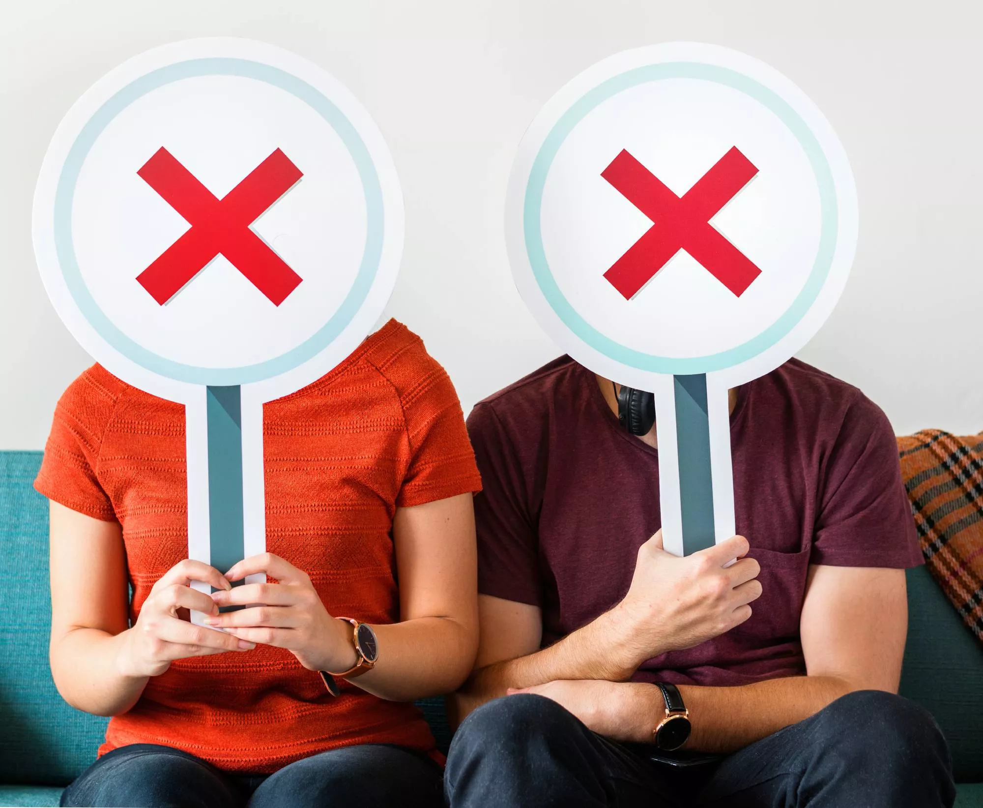 a couple sitting while holding signs with an x mark over their face to show the churn analysis