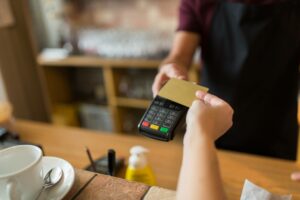 cashier accepting credit card payment by holding out POS terminal for customer to tap card