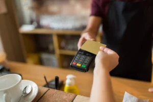 cashier accepting credit card payment by holding out POS terminal for customer to tap card 