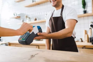 male cashier handing terminal to customer paying with credit card made possible by payment service provider