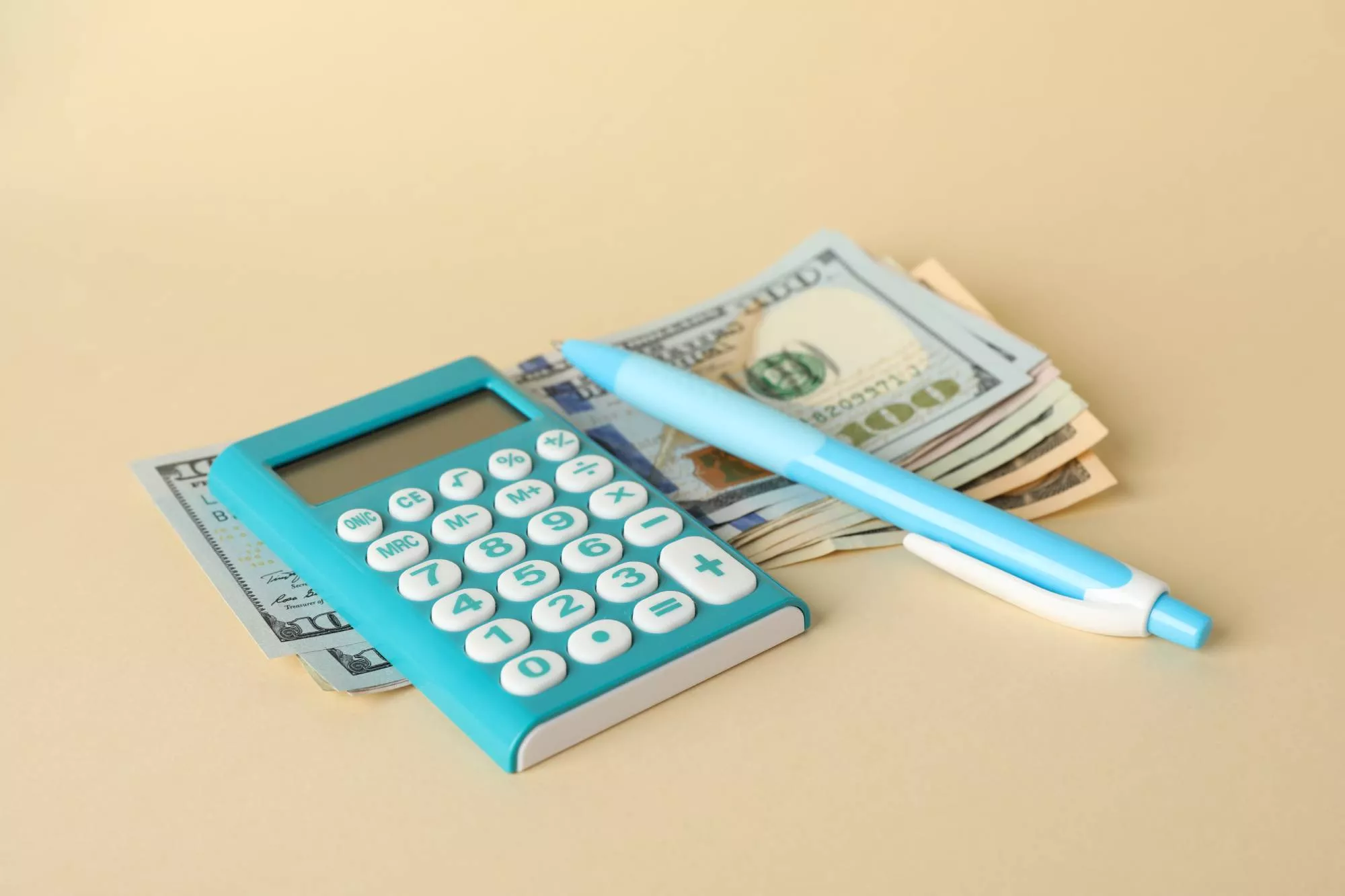 A calculator being used as a business expense tracker on top of a stack of money and next to a pen