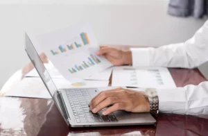 A businessman sitting in front of laptop and holding a paper with graphs and learning how to track business expenses