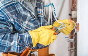 electrician wearing plaid shirt and yellow gloves cutting a wire because he's starting an electrical business