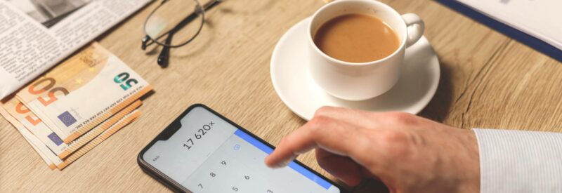 a person calculating stripe fees on phone with a cup of coffee and newspaper
