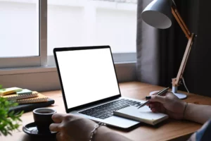 a person holding a pen to a notepad, in front of their laptop, with a cup of expresso deciding if they should use stripe or square for their business