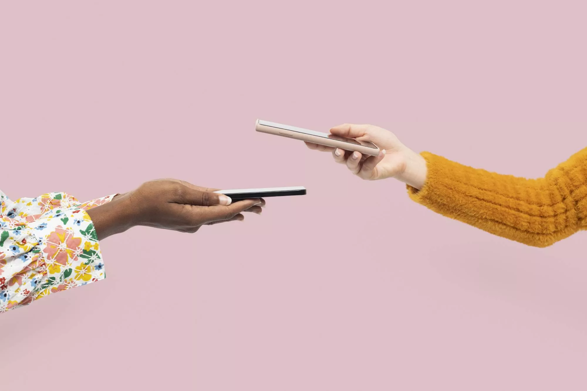 one hand holding a terminal and another hand holding a phone to do contactless payment transaction in front of a pink background after deciding between stripe vs square to pay