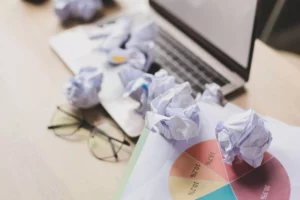 a laptop, glasses, and crumbled business papers on the desk of a businessowner on the TMF list