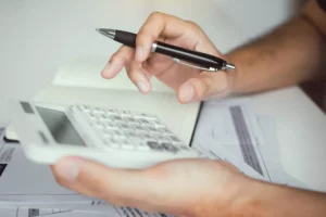 a person going over the break even point formula on a calculator at a desk 