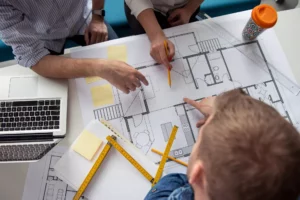 three people pointing business plan examples on a table with rulers a coffee cup and laptop near them