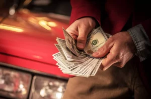 someone holding a bundle of their cash flow while leaning against a car