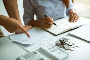 Two people going over their cash flow statement on a desk with cash and coins and a calculator