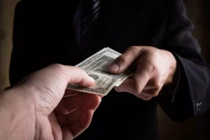 a hand taking dollar bills from another person wearing a black suit after a chargeback vs dispute debate. 