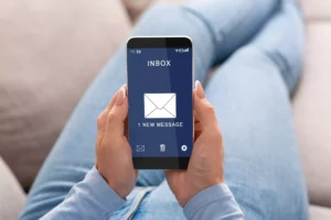 someone laying on a couch with their phone that displays an email from someone who learned to create a newsletter