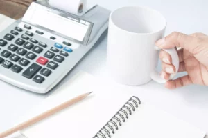 someone who just wrote an expanded accounting equation holding a mug on a desk with office supplies