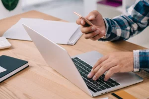 a person at their desk with a laptop and phone searching how to make a newsletter