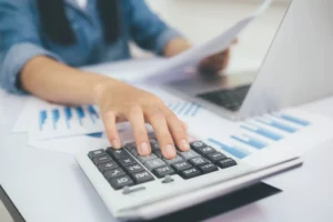 a woman looking over financial documents and typing on calculator to determine an interest rate factor