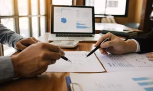 two business partners going over the net profit margin formula on a desk at the office