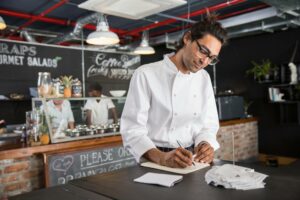 a chef at his restaurant writing down restaurant payment processing on a notepad