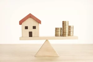 a house made out of mini blocks on a scale with coins to show what is an asset 