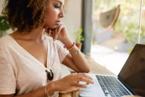 A woman searching on her laptop what is social media marketing while sitting in front of a window.