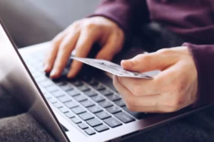 Man, holding credit card, searching on his laptop about chargeback rate