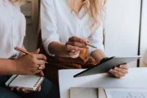 Two women working on marketing social media posts on an ipad and wrtiting out notes