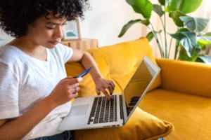 woman sitting on a couch searching on a laptop for a cheap credit card processor