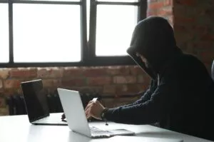 someone in a hoodie sitting at a desk to search up how to tell if a check is fake so they can commit check fraud 