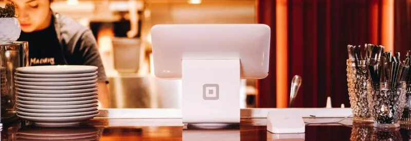 A restaurant employee working while next to a square reader on the counter
