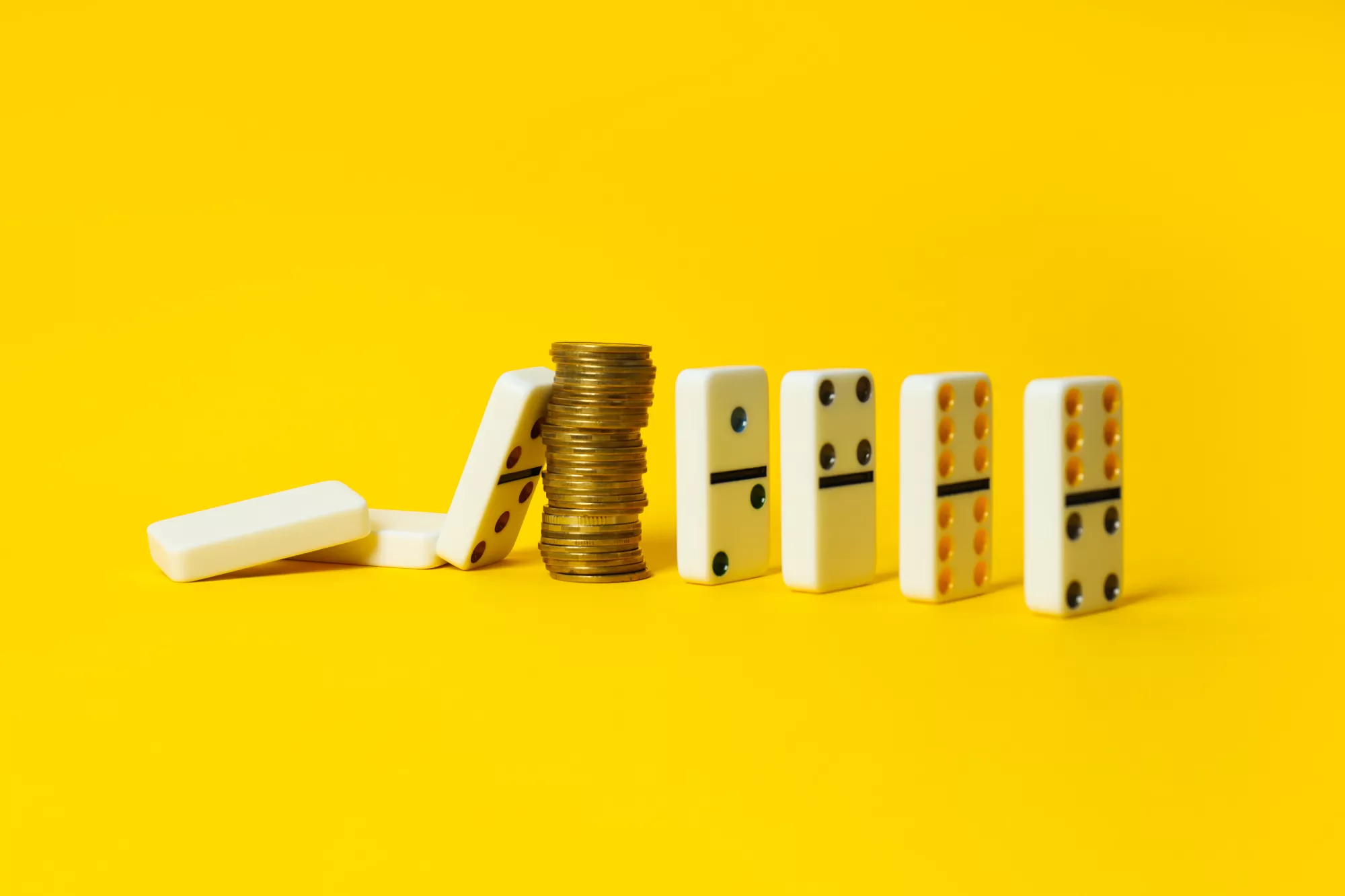 dominos and a stack of change against a yellow background representing recession-proof businesses