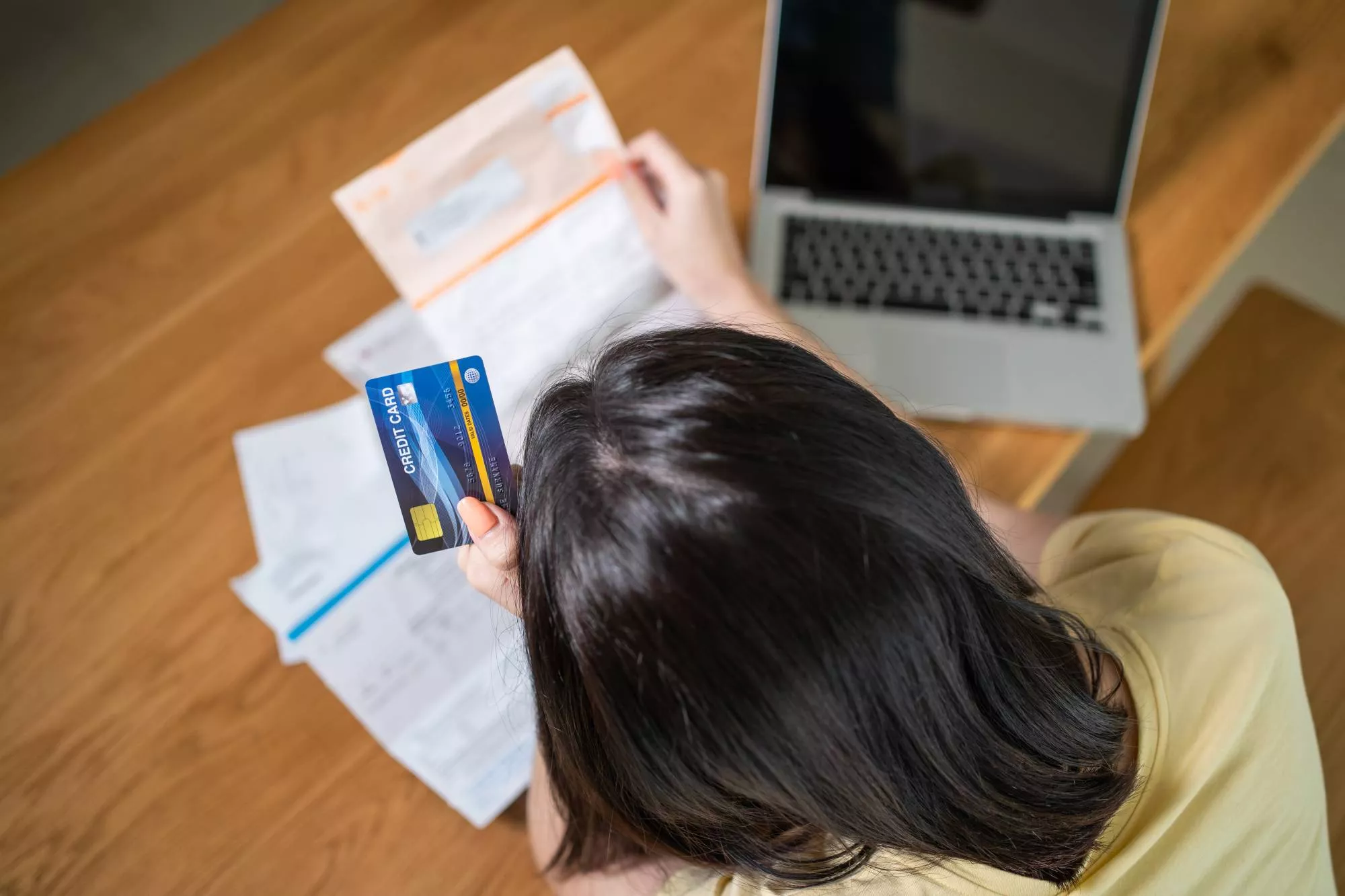 person with black hair holding a credit card and looking at their laptop because they are dealing with an invalid merchant id