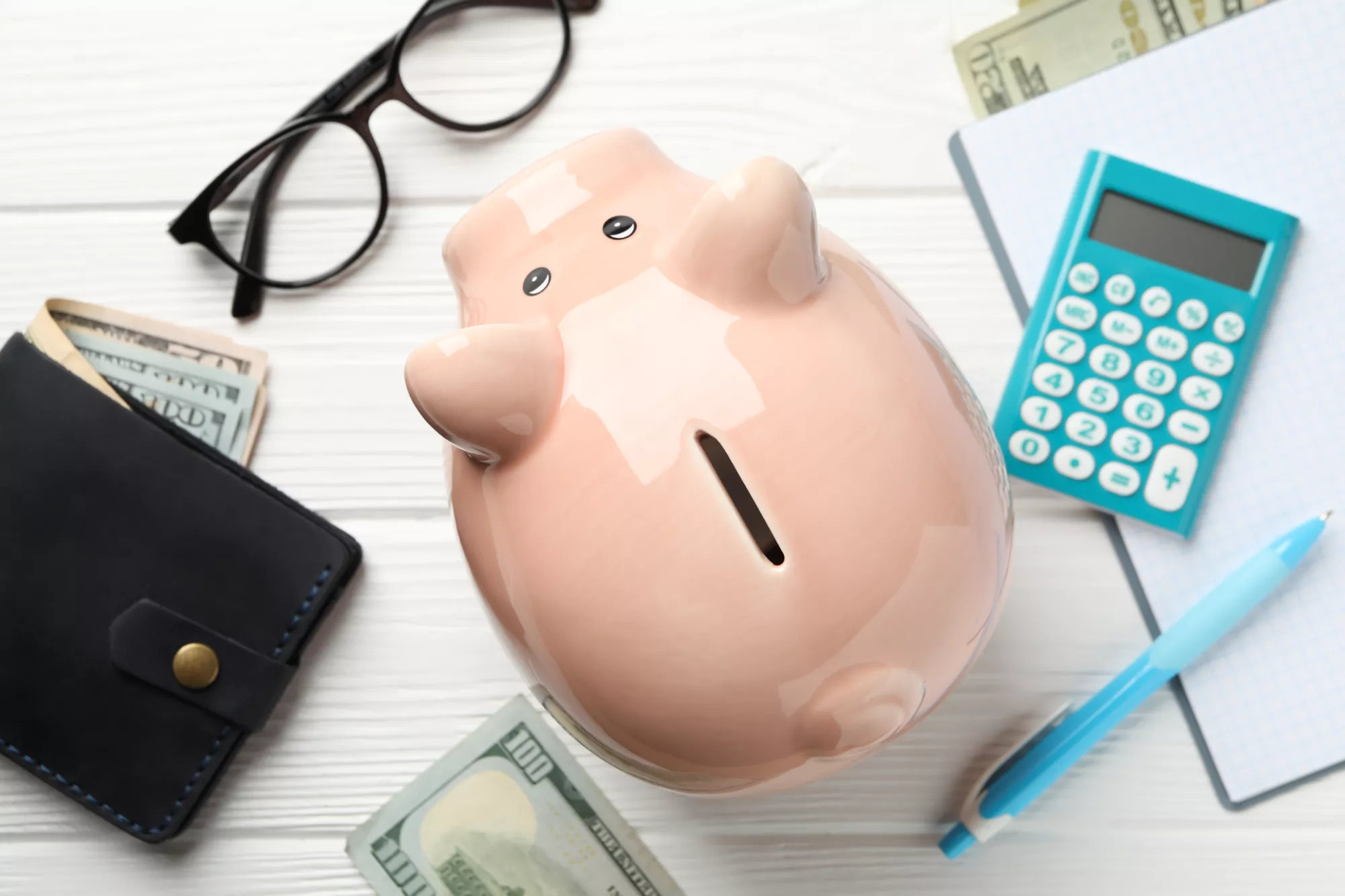 A piggy bank, a calculator and a wallet with money in it to represent saving money in a merchant account reserve balance