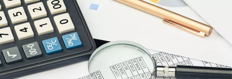 A calculator, a pencil, and a magnifying glass next to a financial document for a merchant account bank