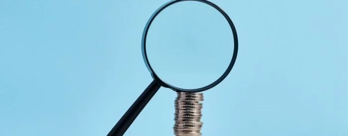 Magnifying glass over a stack of coins in front of blue background to discover if zelle charges a fee for business.