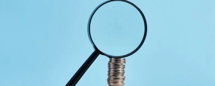 Magnifying glass over a stack of coins in front of blue background to discover if zelle charges a fee for business.