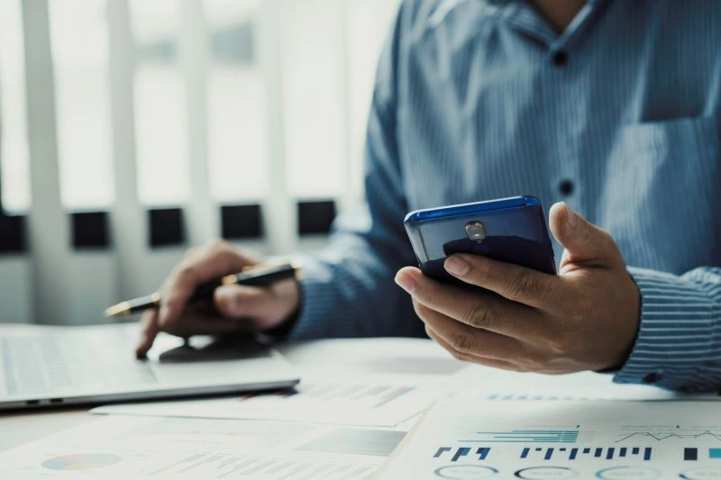 A man at a desk holding a smartphone and depositing an eCheck without printing.