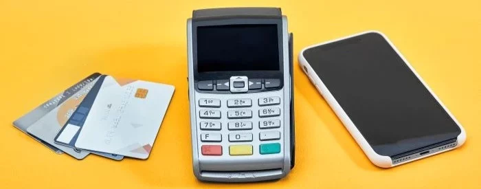 A mobile credit card reader, smarphone, and stack of credit cards on an orange background.