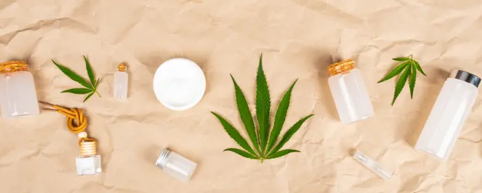 CBD leaves and containers on a sand colored backdrop.