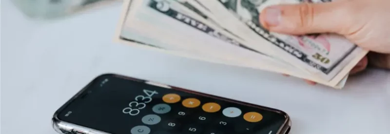 A hand holding multiple five dollar bills over a calculator to determine Cash App business account fees.