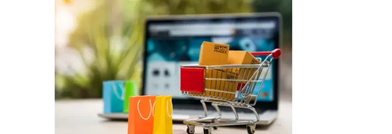 Little shopping cart filled with items bought from selling on shopify in front of laptop