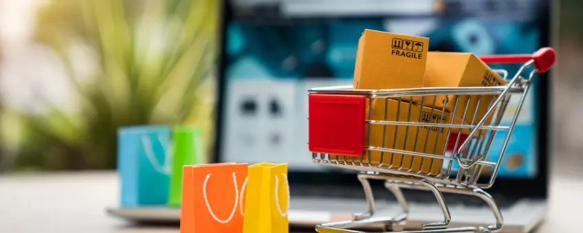 Little shopping cart filled with items bought from selling on shopify in front of laptop