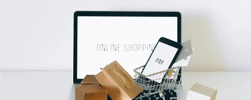 Sellvia vs Shopify: laptop with the words "Online Shopping" across the screen and a smartphone with the word "Pay" across the screen in a mini shopping cart with shopping bags beside it.