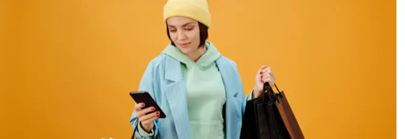 A woman holding shopping bags. She is looking at her smartphone, evaluating Shopify vs Etsy.