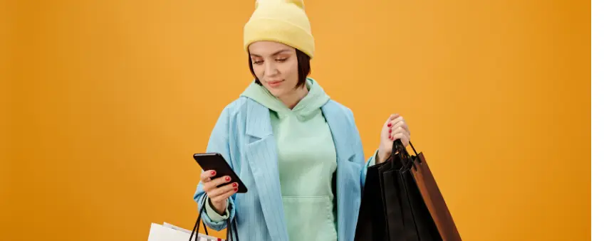 A woman holding shopping bags. She is looking at her smartphone, evaluating Shopify vs Etsy.