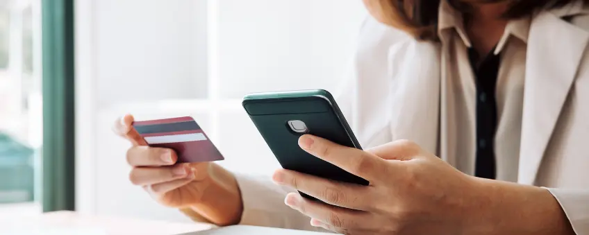 A woman looking at her credit card and cellphone evaluating different payment methods.