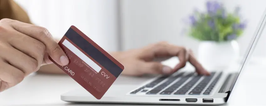 A hand holding a credit card by a laptop, evaluating what a pre-authorization charge is.